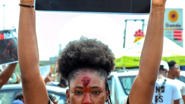 A Black woman with natural hair holds a sign at a protest