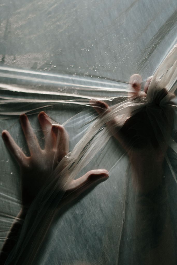 image of two hands of a person trying to escape through an ominous web of plastic