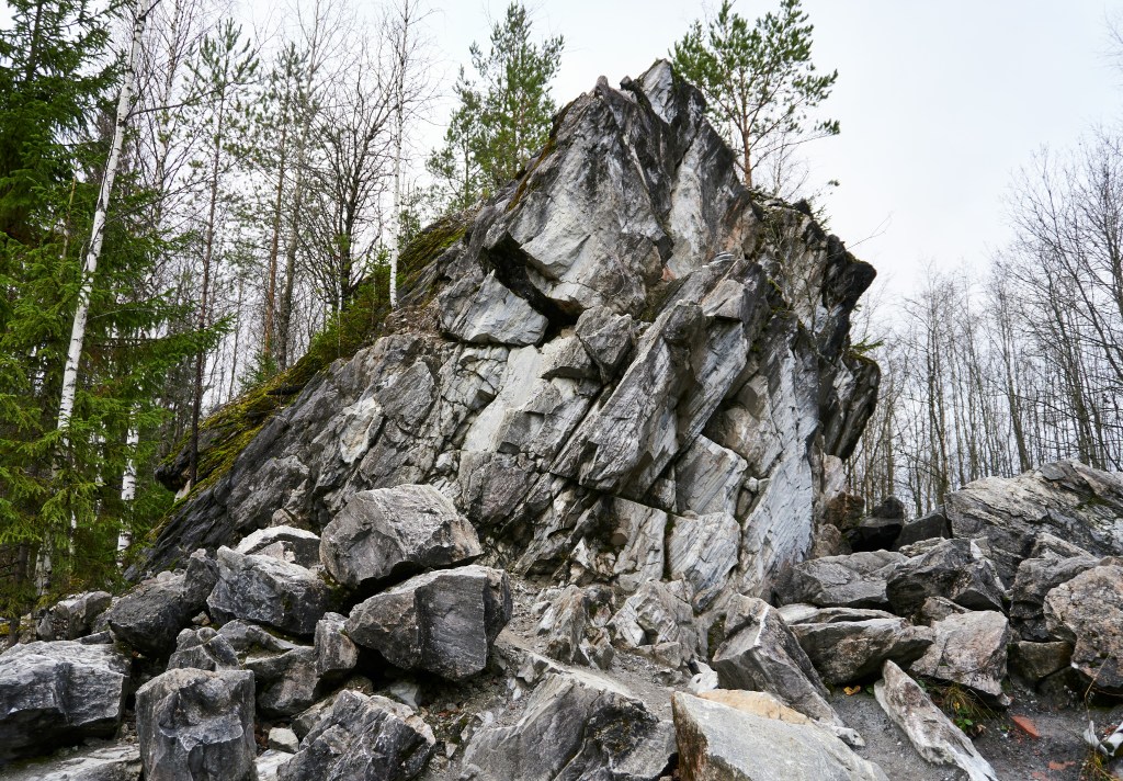 a forest with a close up of a grey mountain splitting into piles of big rocks