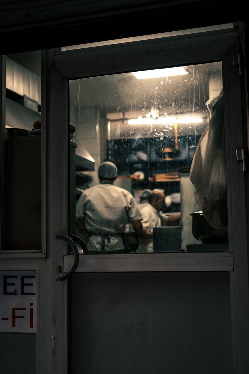 photo of restaurant back of house employees working in a kitchen, taken from the outside through a back door